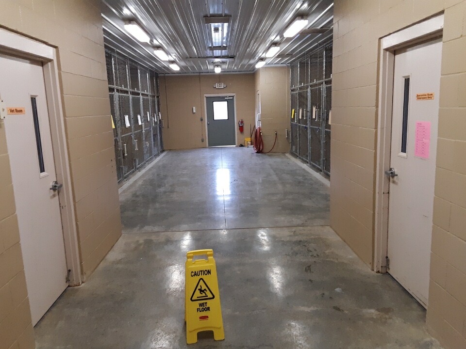 Inside view of the kennel complex with a concrete floor and metal ceiling, with two white doors and one gray door, and a Caution